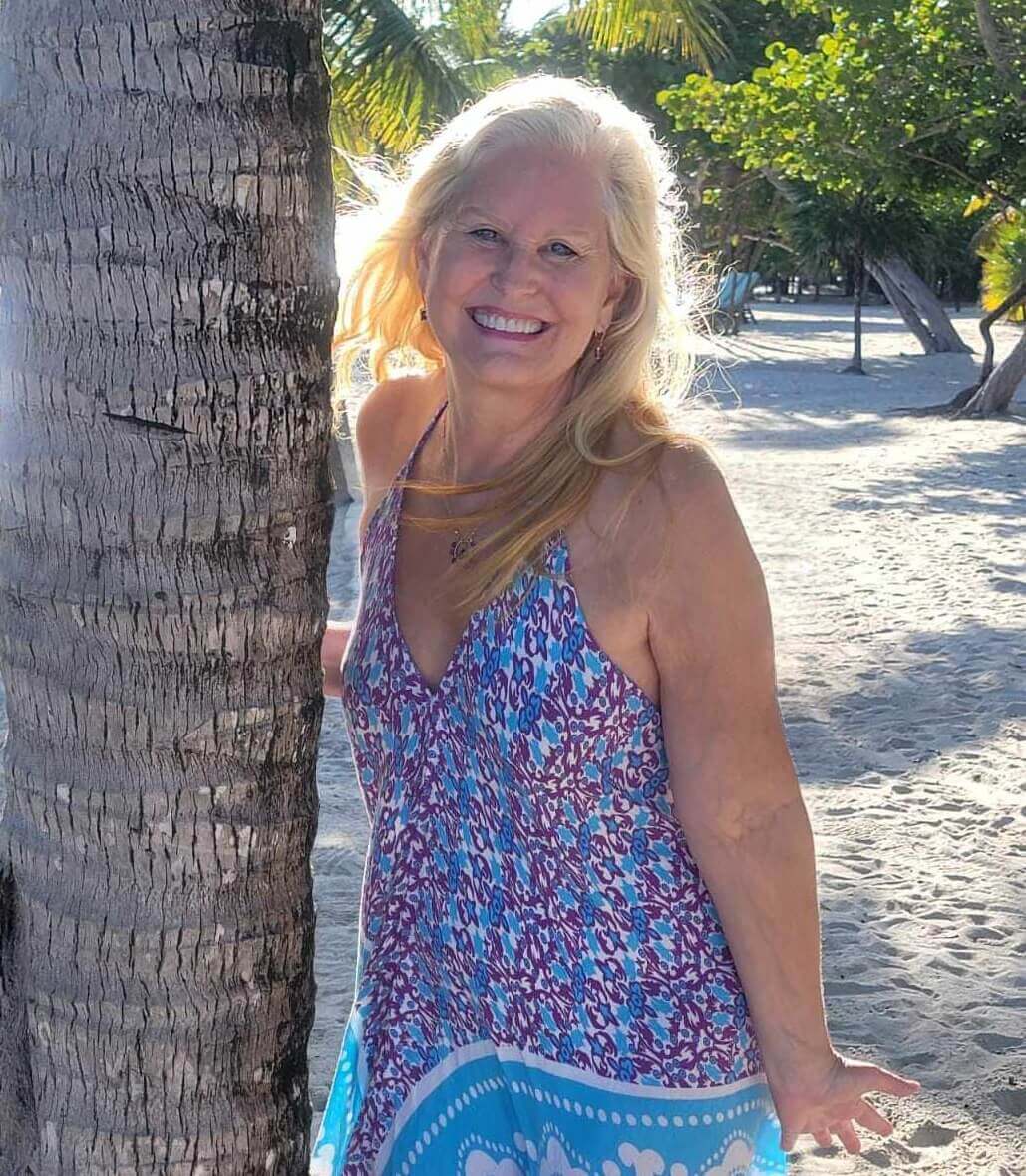 Jyll laughing by a palm tree on the beach in Belize