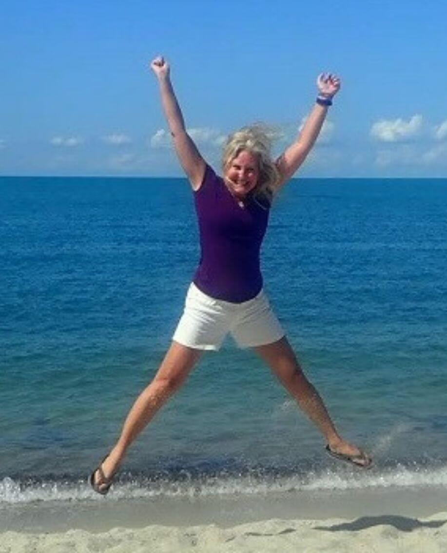 Jyll Hoyrup jumping on a Belize beach smiling with arms raised