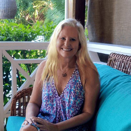 jyll-smiling-energy-healer Jyll Hoyrup standing on a Belize balcony surrounded by tropical plants, smiling in a purple dress